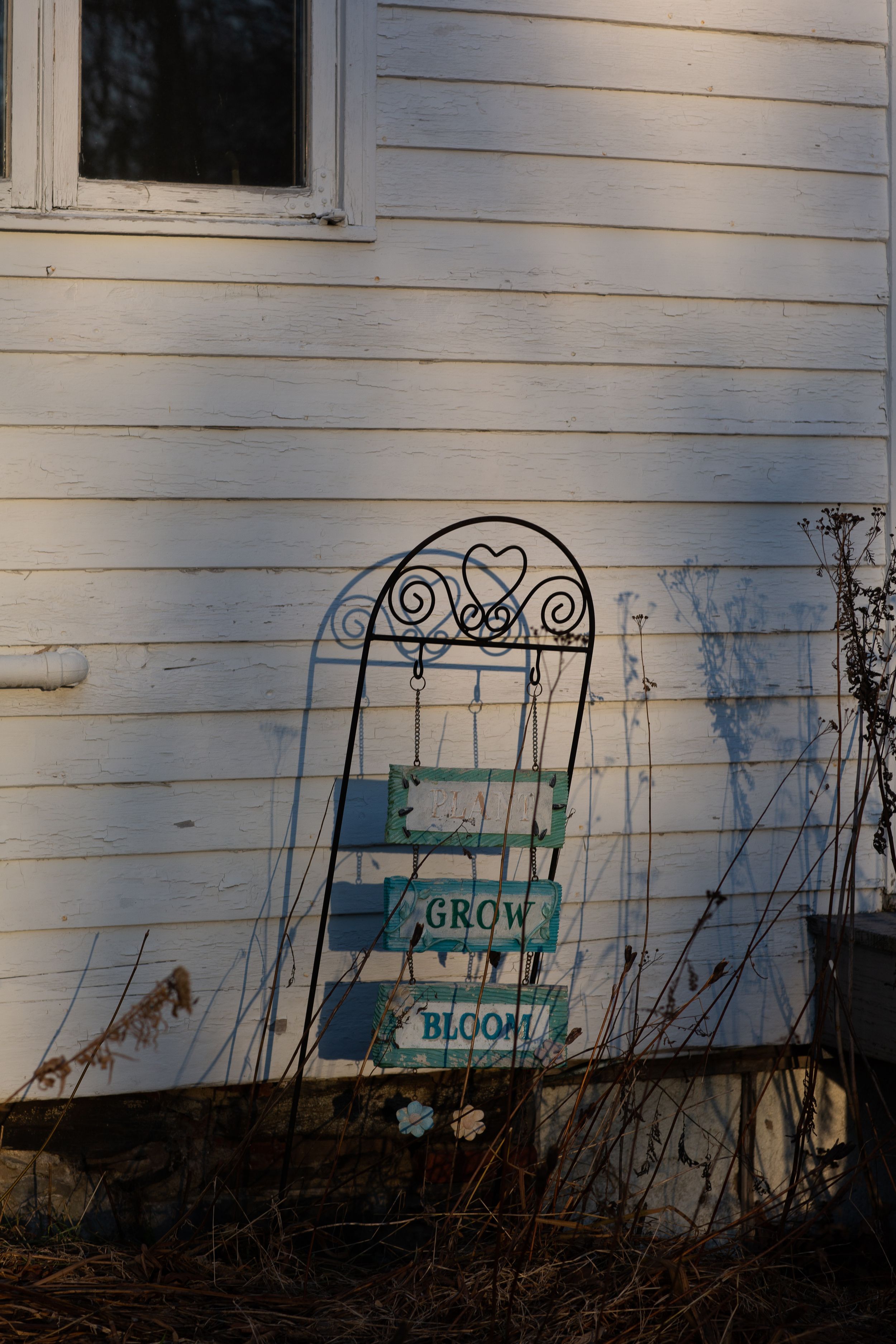 A decorative metal garden bench and welcome sign cast shadows on a white house exterior.