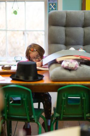 Green plastic chairs line up at wooden tables in a bright classroom setting.