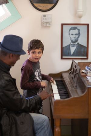 An upright piano sits against a wall decorated with vintage portraits.