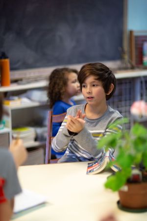 A student sitting at a desk in a classroom with a chalkboard visible in the background.
