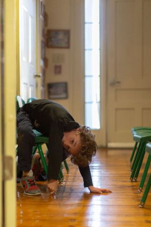 People bending down to examine something on a wooden floor between green chairs.