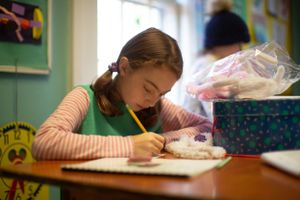 Students focused on writing at their desks in a bright classroom setting.