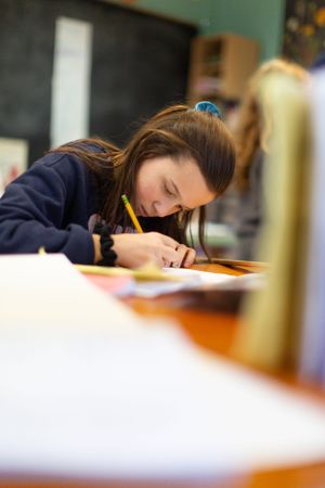 Student concentrating on schoolwork at desk in classroom setting.