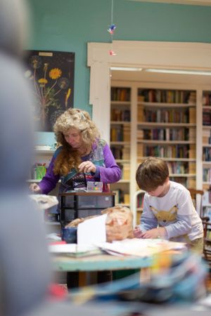 Students engaged in classroom activities with bookshelves and learning materials visible.