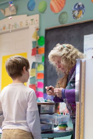 Classroom scene showing students and teacher working at desks with colorful wall decorations.