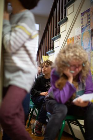 Students sit in a classroom with colorful artwork displayed on the wall behind them.
