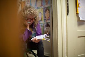 Person in purple sweater reads while sitting near a wall decorated with children's artwork.