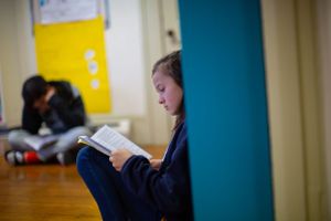 Student reads quietly in a corner of a classroom with hardwood floors.