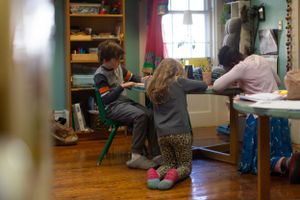 Students sit at desks in a colorful classroom with wooden floors and bookshelves.