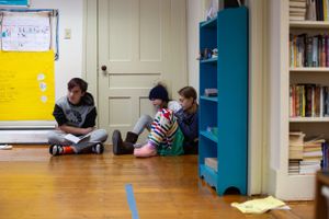 Students gather on the floor near a blue bookshelf in a classroom setting.