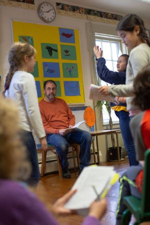 A classroom discussion takes place with colorful artwork displayed on yellow bulletin boards.