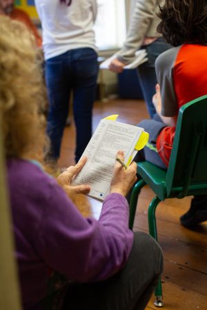 A person holds a document while seated in a green chair during a classroom session.