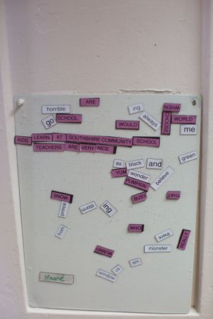 A white board displays scattered magnetic words including 'school', 'community', and 'teacher'.