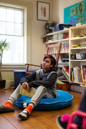 Student relaxing on a blue cushion in a classroom setting with wooden floors.