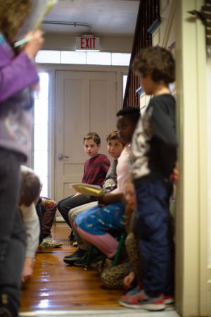 Students sitting on wooden floor near exit door during classroom activity.