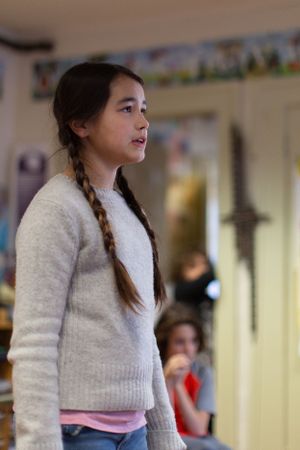 Student in cream sweater standing in classroom during presentation.