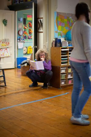 Classroom scene with person reading document while another stands nearby.