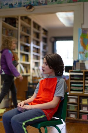 Student in red vest sitting in green chair in classroom setting.