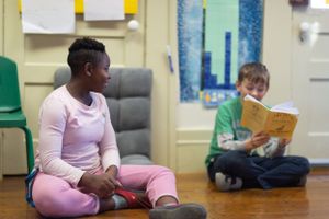 Children sitting and reading books on hardwood floor in classroom.