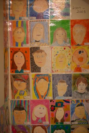 Wall display of colorful student self-portrait artwork in warm tones.