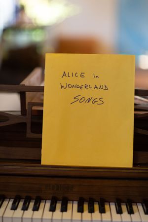 Yellow note cards on a piano keyboard spelling out 'Alice in Wonderland Songs'.