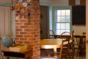 A classroom interior with exposed brick walls, wooden chairs and large windows.