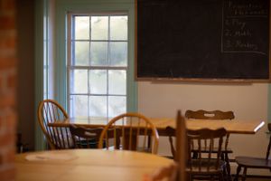 Sunlit classroom with wooden furniture and brick walls visible through large windows.