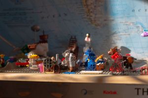 Collection of small toy figures and objects displayed on a shelf with a map background.