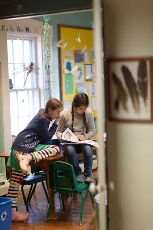 Two students reading together at green chairs in a classroom with decorated walls.