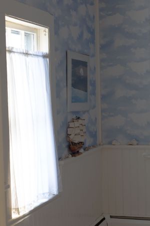 Room with cloud-patterned wallpaper, white curtained window, and nautical decorations.