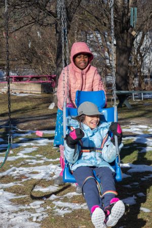 Person enjoying a winter day on a blue playground swing with snow on the ground.