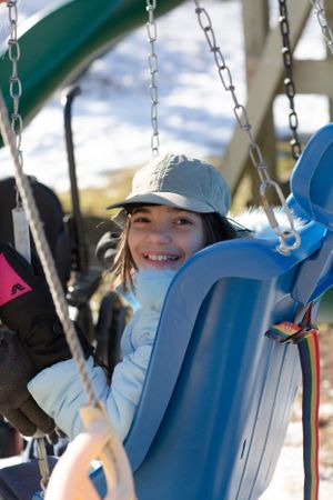 Person swinging joyfully on a blue playground swing on a sunny winter day.