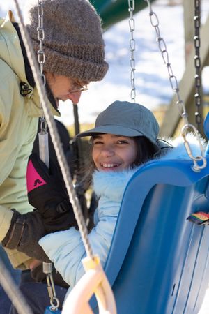 Person wearing winter clothing enjoying a playground swing on a bright day.