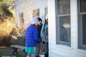People in winter clothing gathered outside a white building on a sunny winter day.