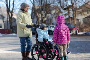 People gather around a wheelchair on a snowy winter path.