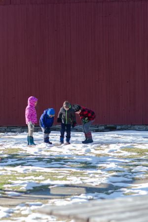 Children play in the snow near a burgundy colored wall on a winter day.