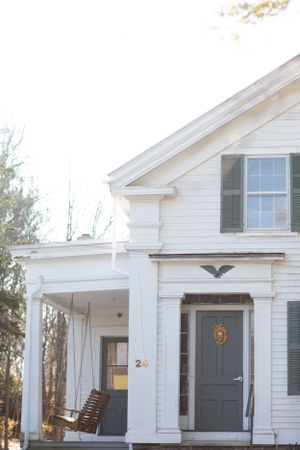 White farmhouse with gray door and porch swing in winter sunlight.