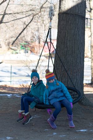 Two people swinging on tree swings in a snowy winter setting.