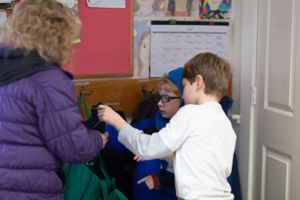 People in winter coats pointing and interacting in an indoor classroom setting.