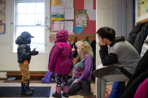 Students hanging up coats and organizing boots in school entrance hallway.
