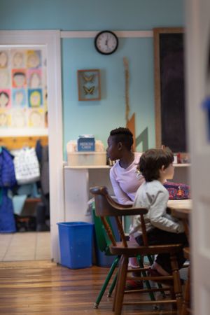 Students seated at wooden chairs in a classroom with light blue walls and artwork displays.