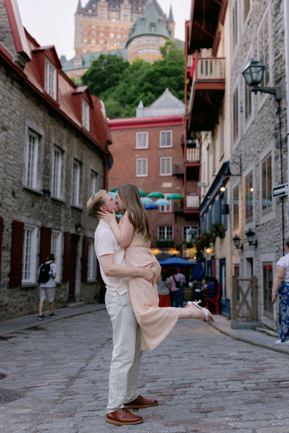 Couple kissing on cobblestone street in Old Quebec City with Chateau Frontenac in background.