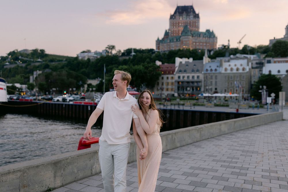 Couple walking along Quebec City waterfront with Chateau Frontenac at sunset.