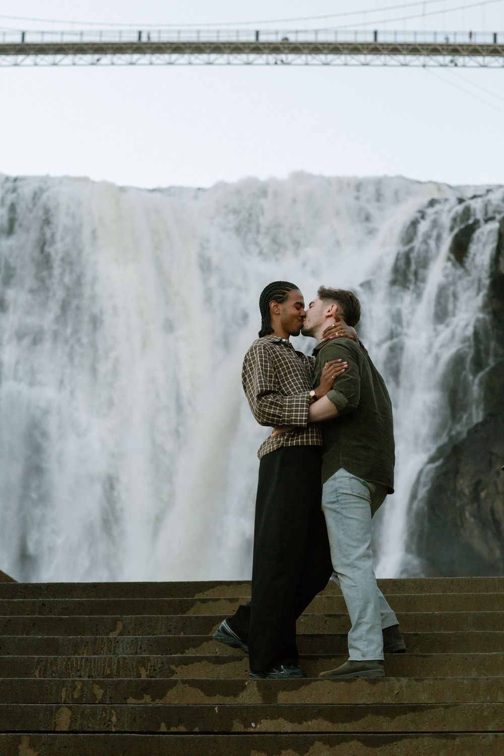 Couple kissing on stone steps in front of a dramatic waterfall backdrop.