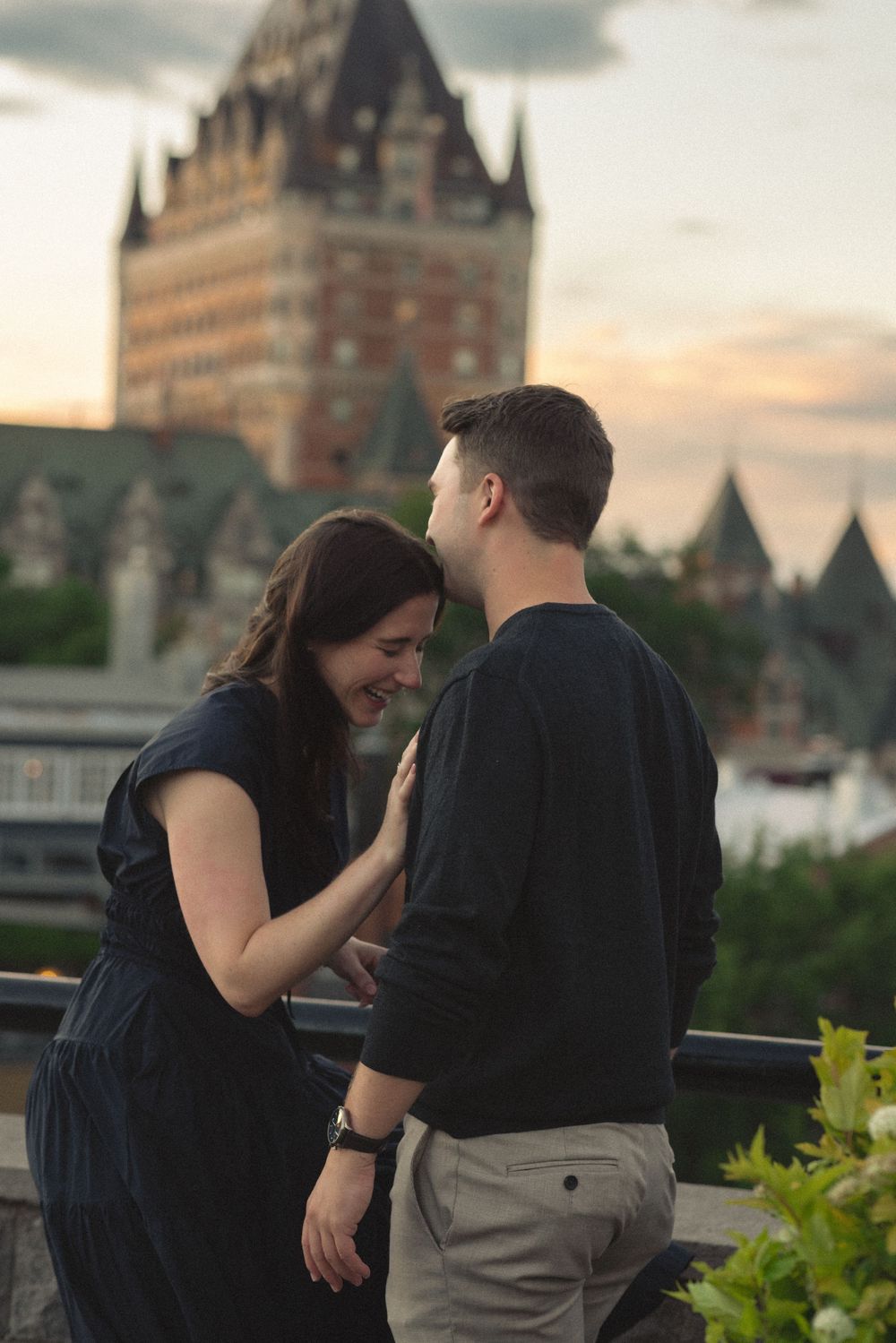 Couple sharing a romantic moment on a terrace with Chateau Frontenac in Quebec City at sunset.