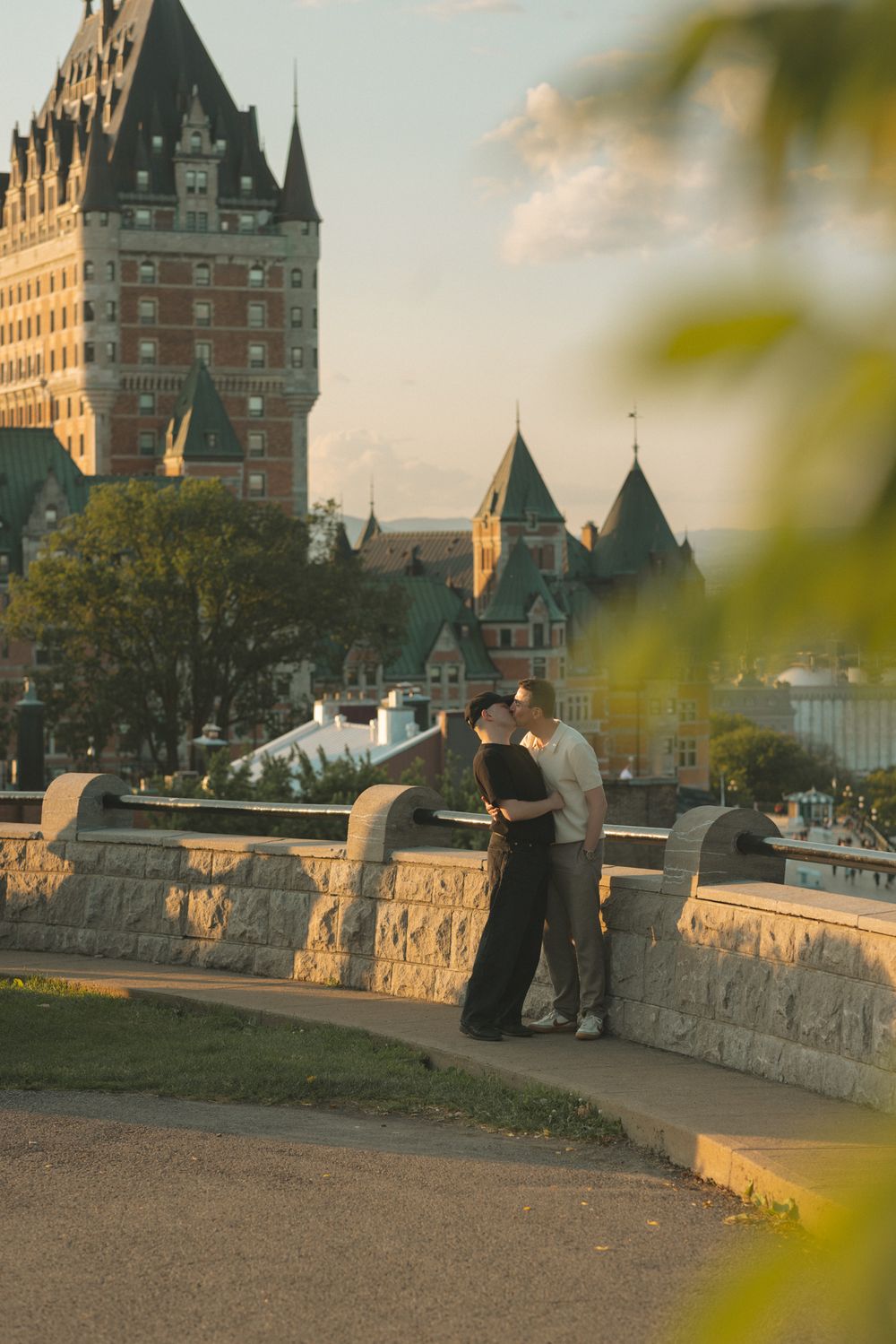 Couple embracing at dusk near Chateau Frontenac in Quebec City, with golden light and lush greenery.