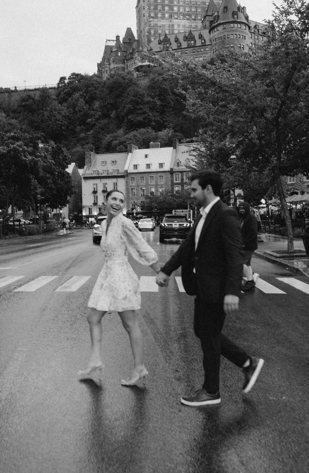 Black and white photo of a couple holding hands crossing a street with Chateau Frontenac in Quebec City background.