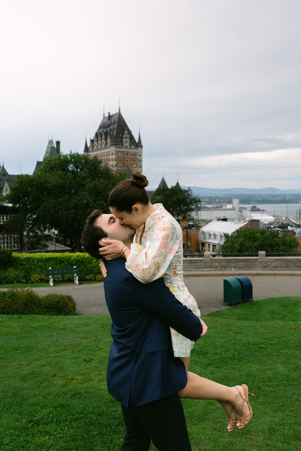 Couple sharing a romantic kiss in front of Chateau Frontenac in Quebec City on a cloudy day.