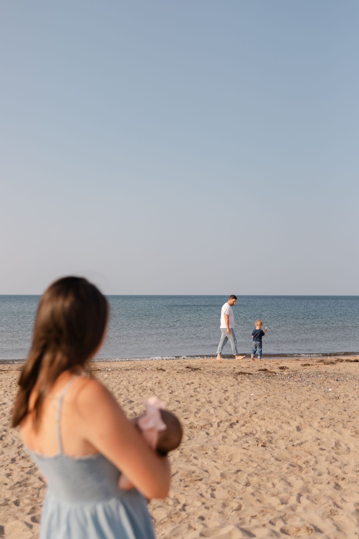 People enjoying a peaceful day at the beach with calm waters and sandy shore on a clear day.