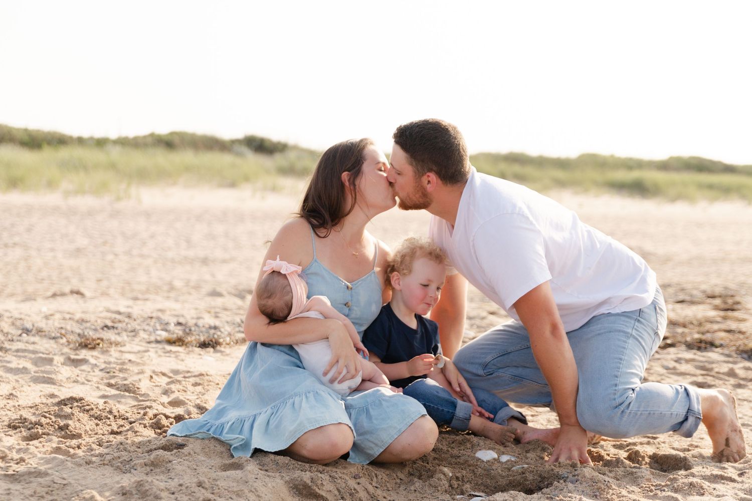 A family of four sharing a tender moment together while sitting on the beach during sunset.